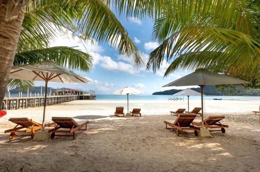 Wooden lounge chairs and umbrellas are set up on a sandy beach under palm trees, facing the ocean—perfect for relaxing after a PADI scubadive beneath the nearby pier under a partly cloudy sky. Wooden lounge chairs and umbrellas are set up on a sandy beach under palm trees, facing the ocean—perfect for relaxing after a PADI scubadive beneath the nearby pier under a partly cloudy sky.