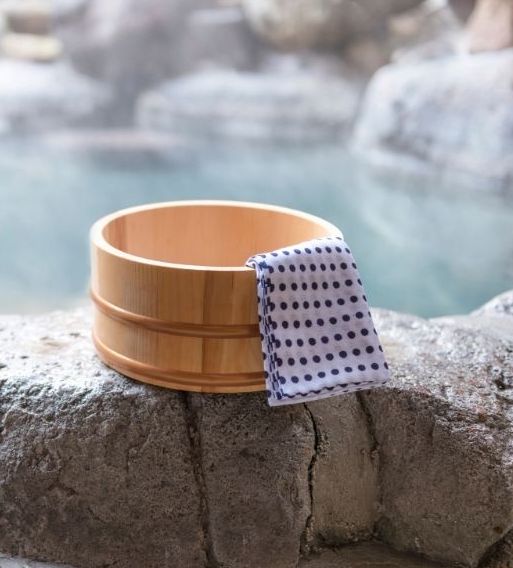 Traditional Japanese onsen setting with wooden bath and towel beside natural hot springs—ideal for spa vacations for adults.