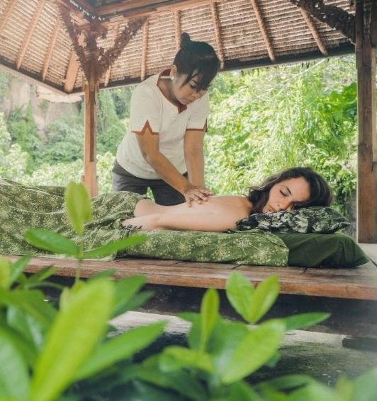 Outdoor massage at a wellness retreat in Thailand surrounded by jungle greenery and traditional wooden pavilion.